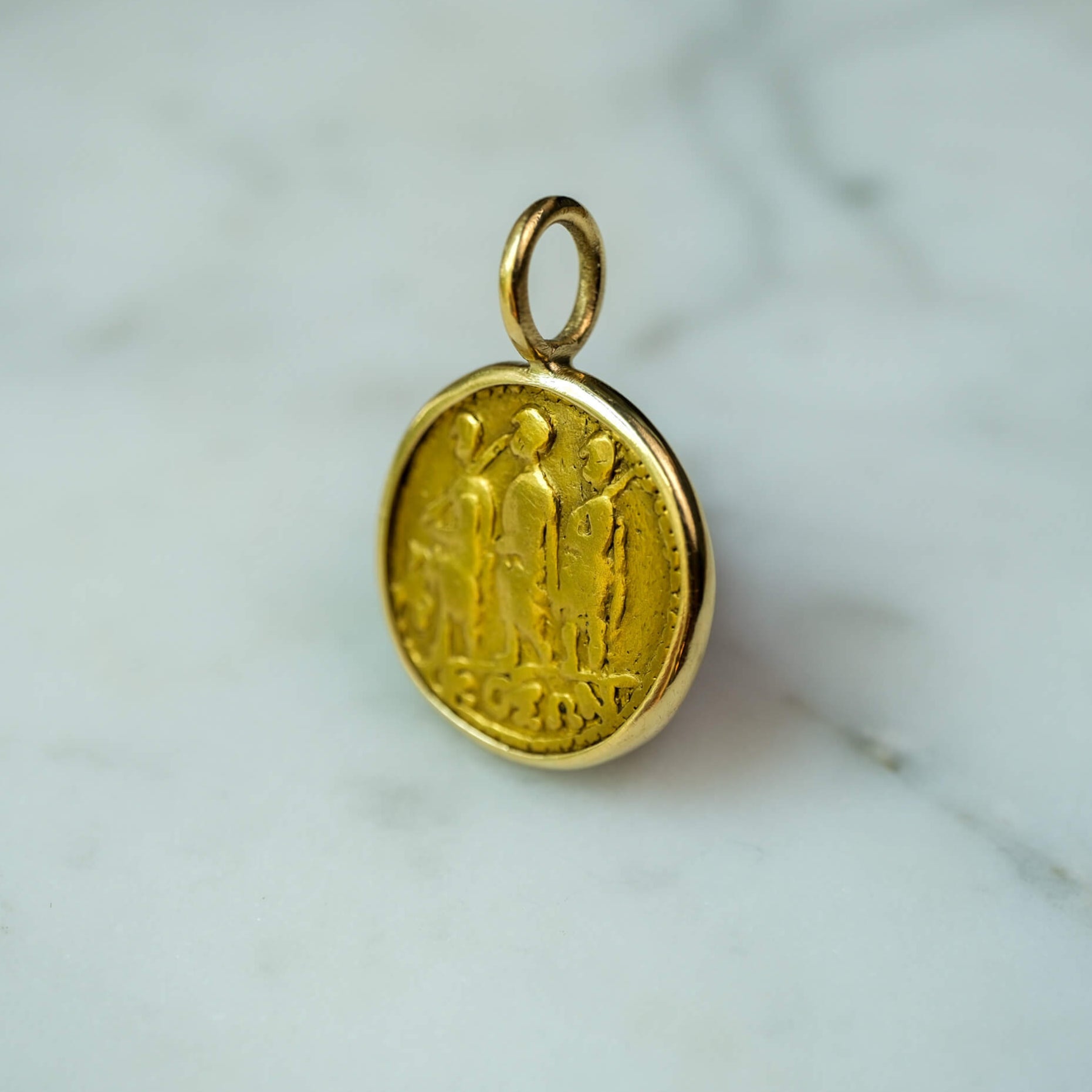 Gold pendant with intricate design on a marble surface